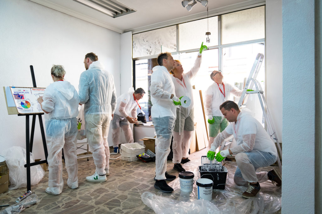 A group of people in white lab coats painting.
