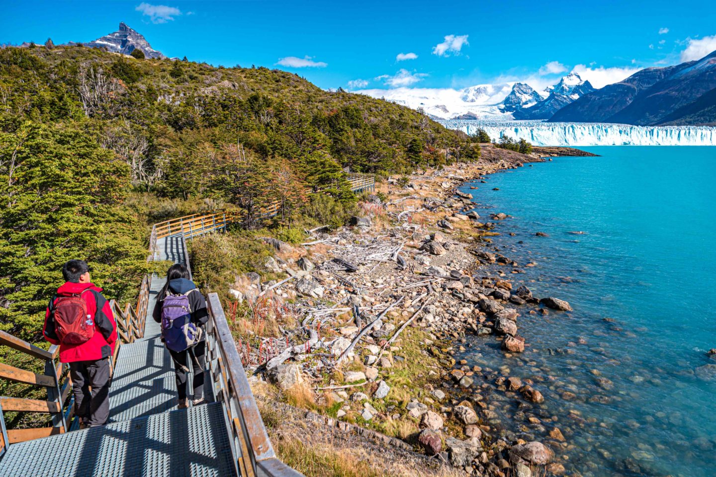 Tourist on boardwalk beside a lake andwith a green forest on the left.
