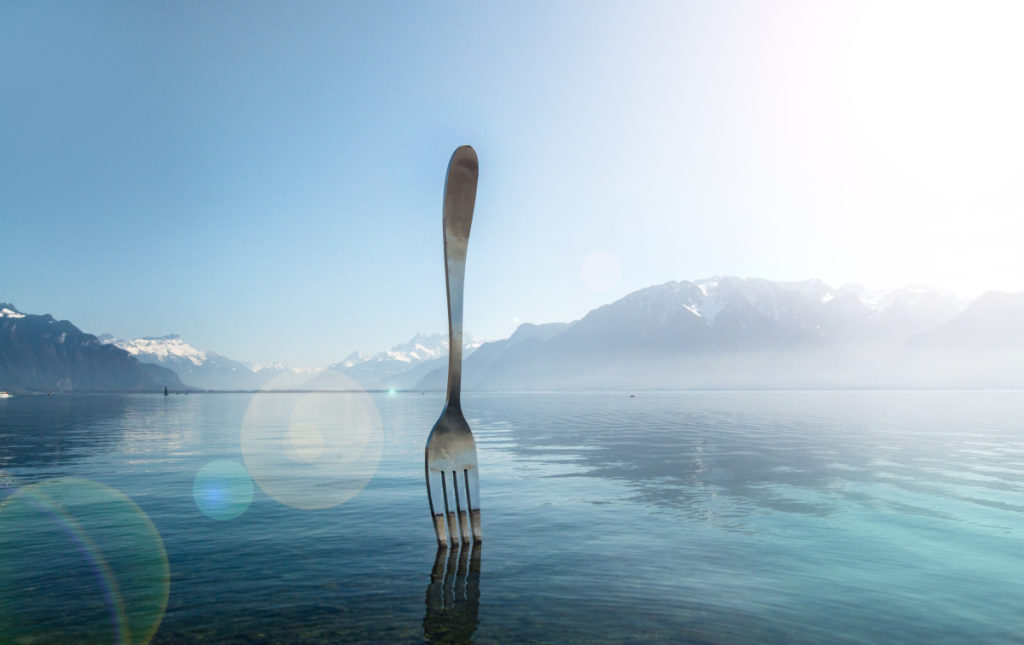 Sunny day at Lake Geneva by "The Fork of Vevey," a modern installation art piece, against the backdrop of the Swiss Alps on a clear and bright autumn day.