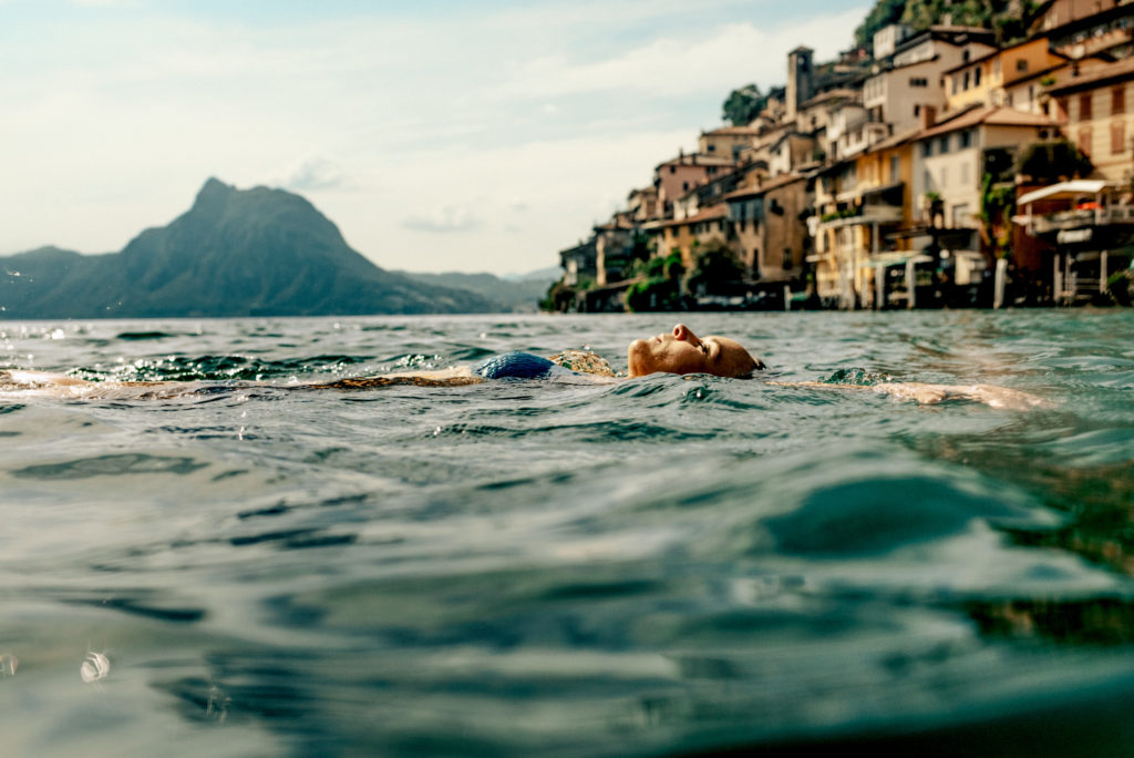 Young woman floating in refreshing lake in Switzerland, Ticino.