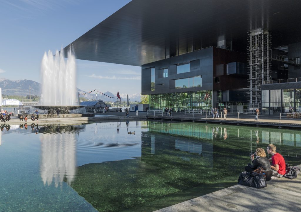 A beautiful building with a fountain where a duo is enjoying the soothing sound of flowing water.