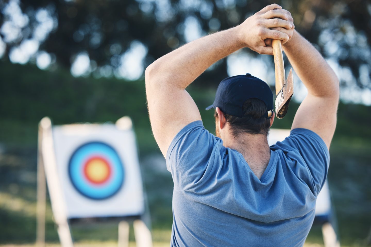 A man practicing axe throwing at a target in a wooded area, preparing for a competition.