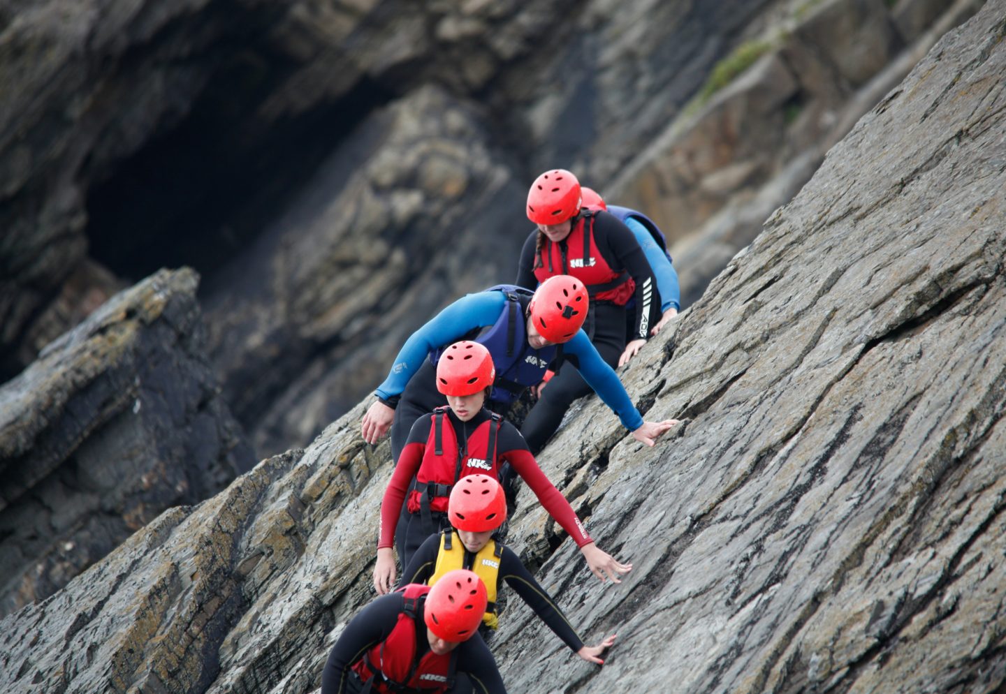 A staycation coasteering group scrambling across the rocks at the Isle of Skye, wearing wetsuits and helmets.