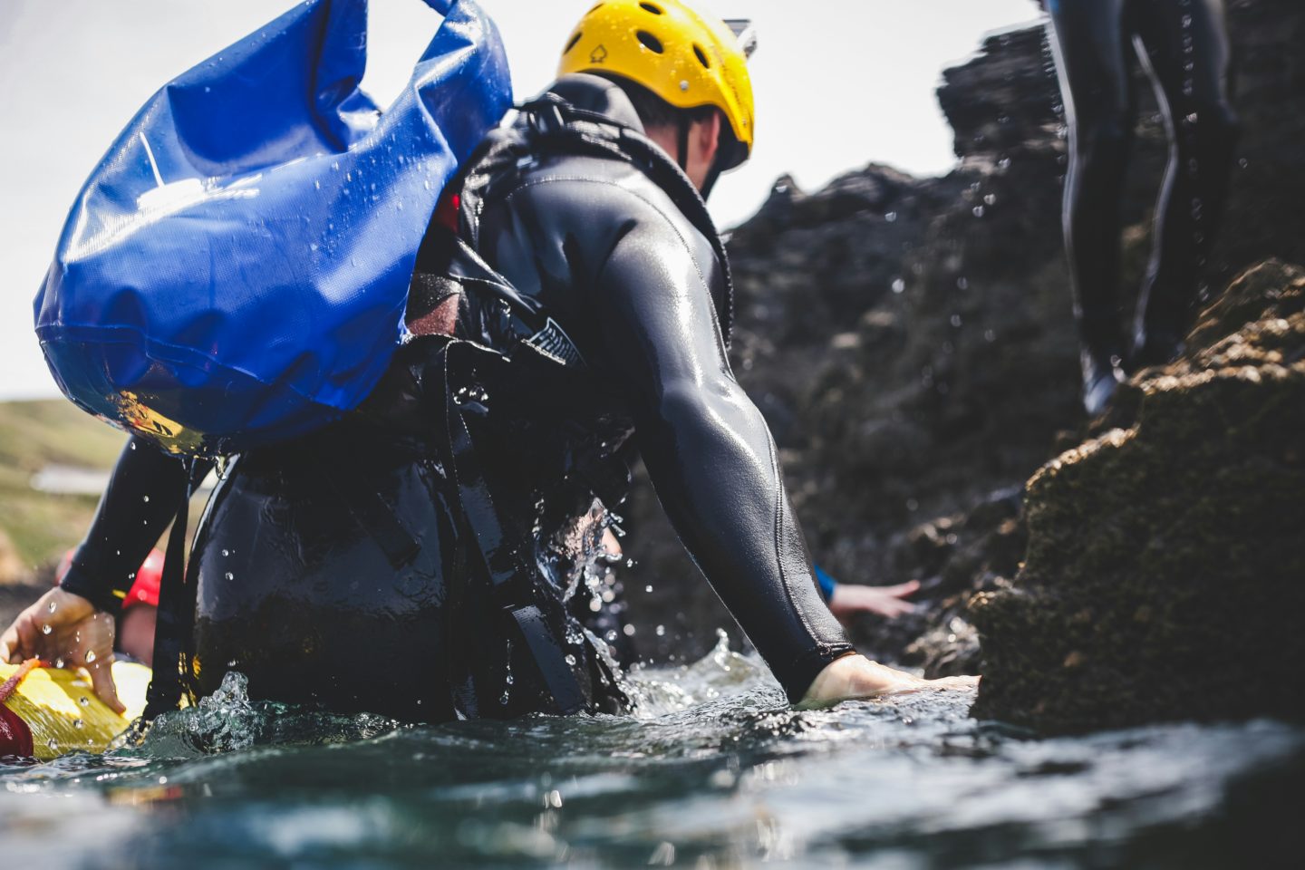 A coasteering guide exiting the sea at the Isle of Skye, wearing a wetsuit and helmet.
