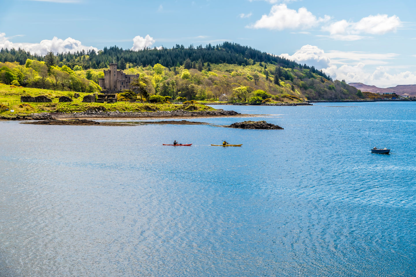 Scenic view of Loch Dunvegan on the Isle of Skye, surrounded by green hills and rocky islets under a partly cloudy sky.