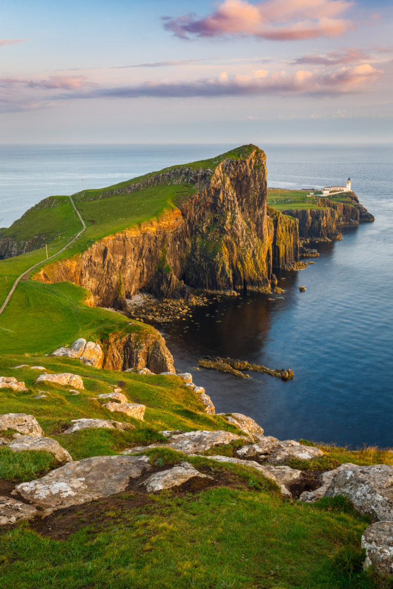 Sunset over Neist Point Lighthouse on the Isle of Skye, with dramatic cliffs and colorful sky reflecting on the ocean.