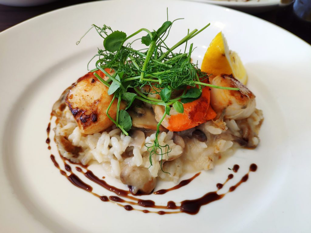 Seared scallops served with a gourmet sauce and herbs, beautifully plated at a restaurant in Portree, Isle of Skye.