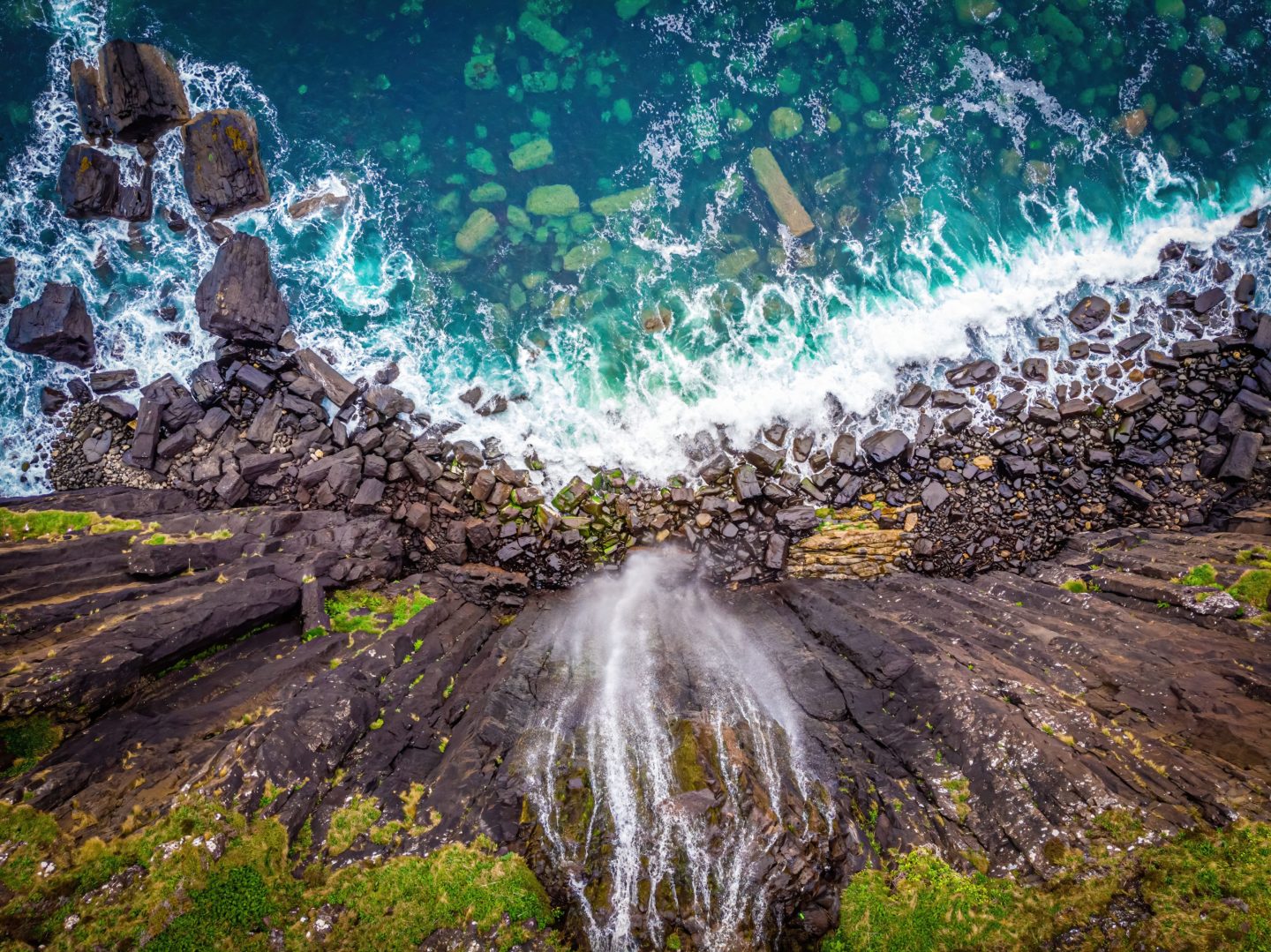 Aerial view of the Isle of Skye's dramatic coastline with cliffs, a waterfall, and a rainbow over the Atlantic Ocean.