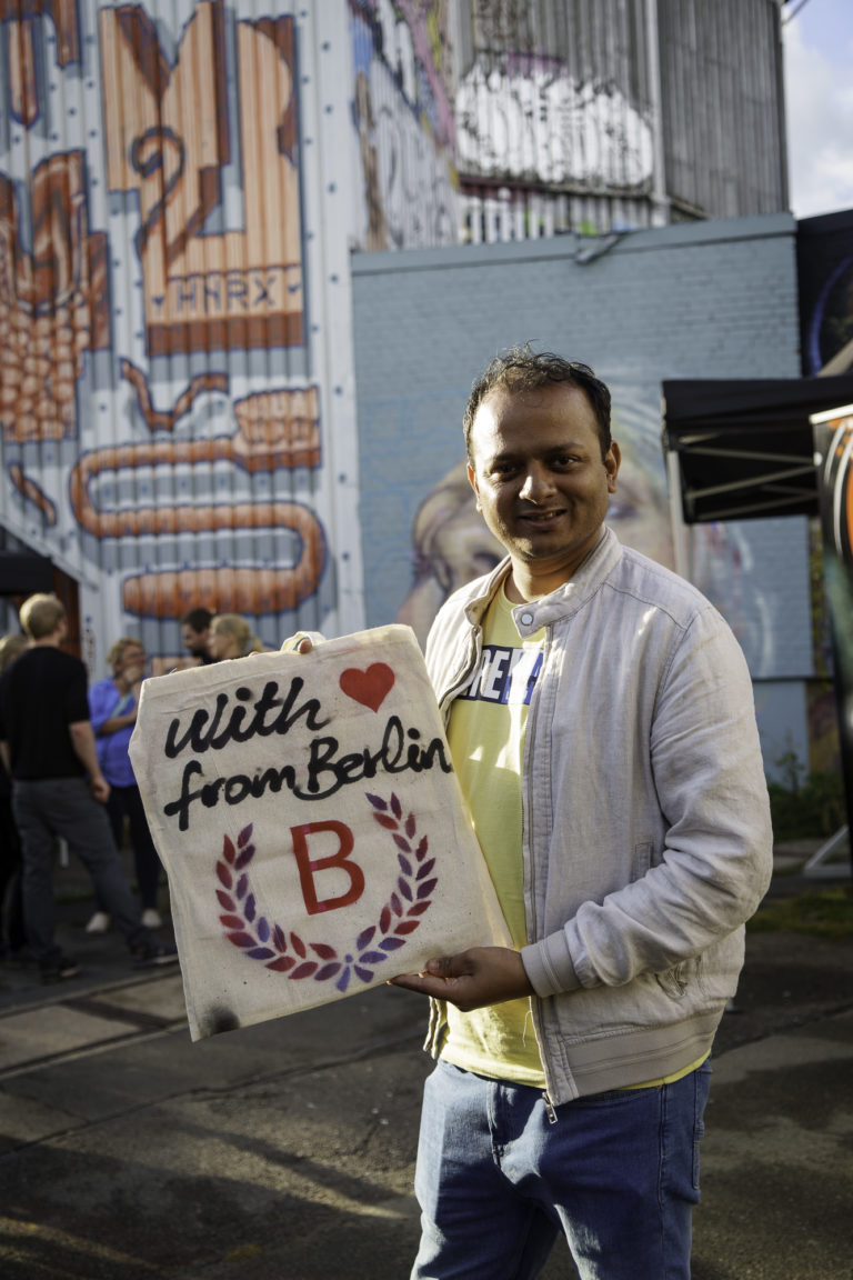 A man holds his self-designed jute bag smiling at the camera at an event in Berlin.