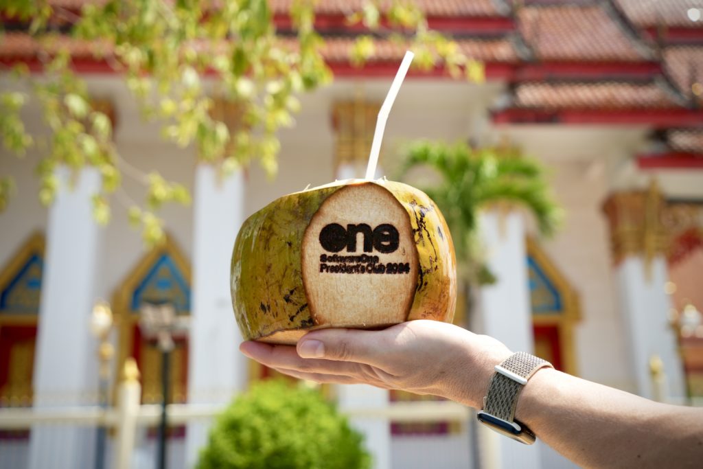 One hand holds a branded coconut with the client's logo during an event in Phuket, Thailand.