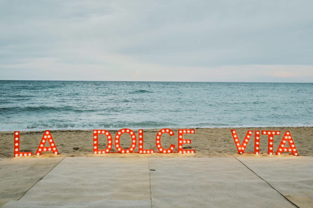 The logo of a private event in Puglia, Italy stands on the beach with the sea in the background.