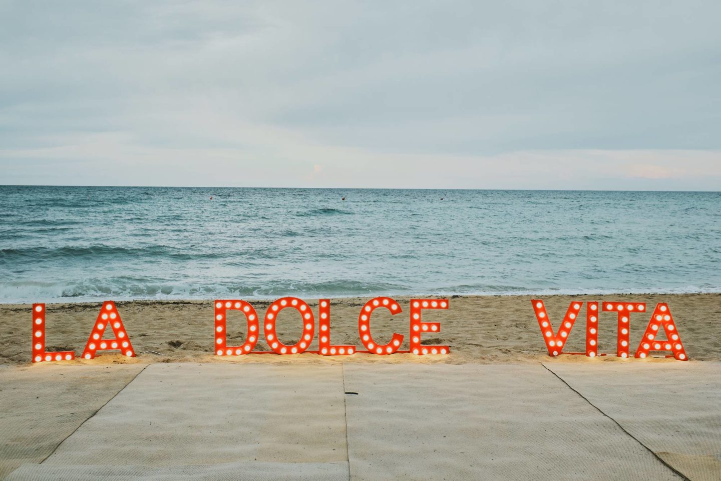 The logo of a private event in Puglia, Italy stands on the beach with the sea in the background.