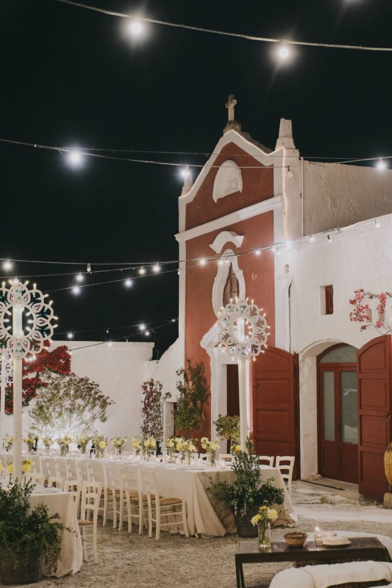Long tables stand under fairy lights in the piazetta where a dinner is held during a private event in Puglia, Italy.