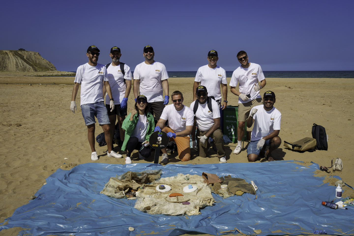 A group of people posing infront of trash they picket up at the beach in Turkey during a beach clean up during a CSR project